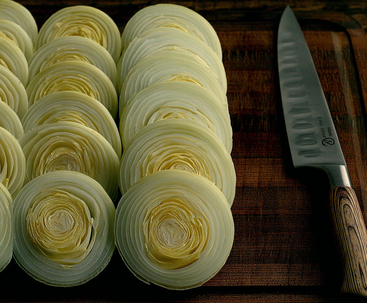 A knife is on a cutting board with onions.