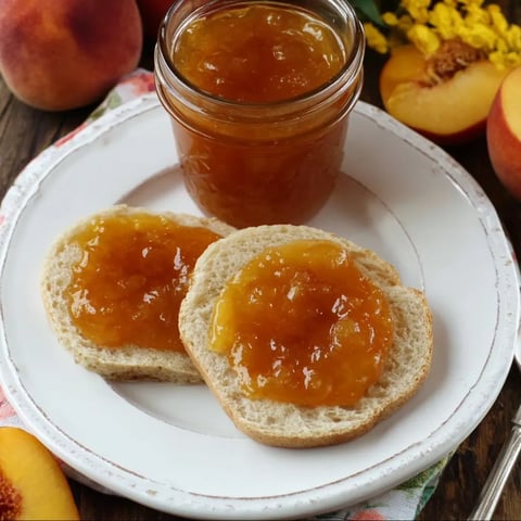 Two slices of bread with peach jam on a white plate.