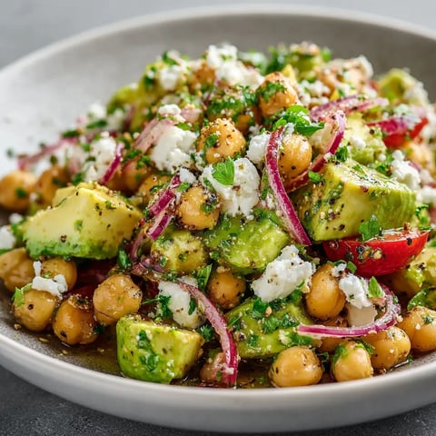 A bowl of food with chickpeas, avocado, tomatoes, and onions.