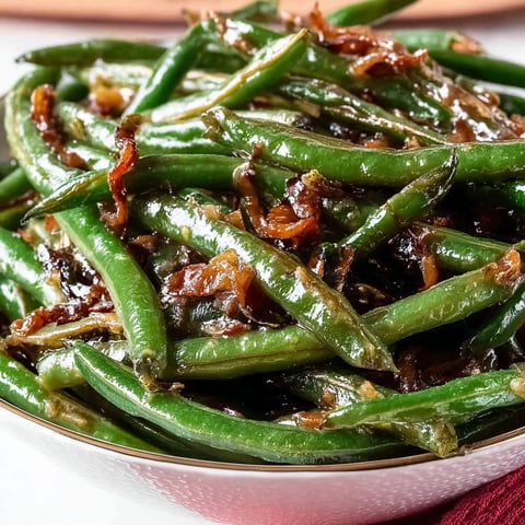 A plate of green beans with a brown sauce.