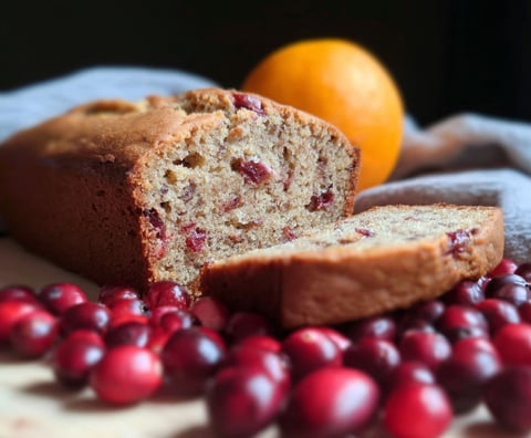 A loaf of bread with a slice missing and an orange beside it.