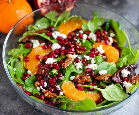 A bowl of salad with oranges and pomegranate.