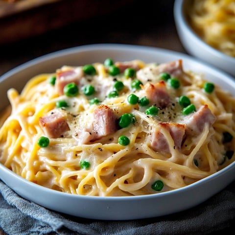 A bowl of pasta with ham and peas.